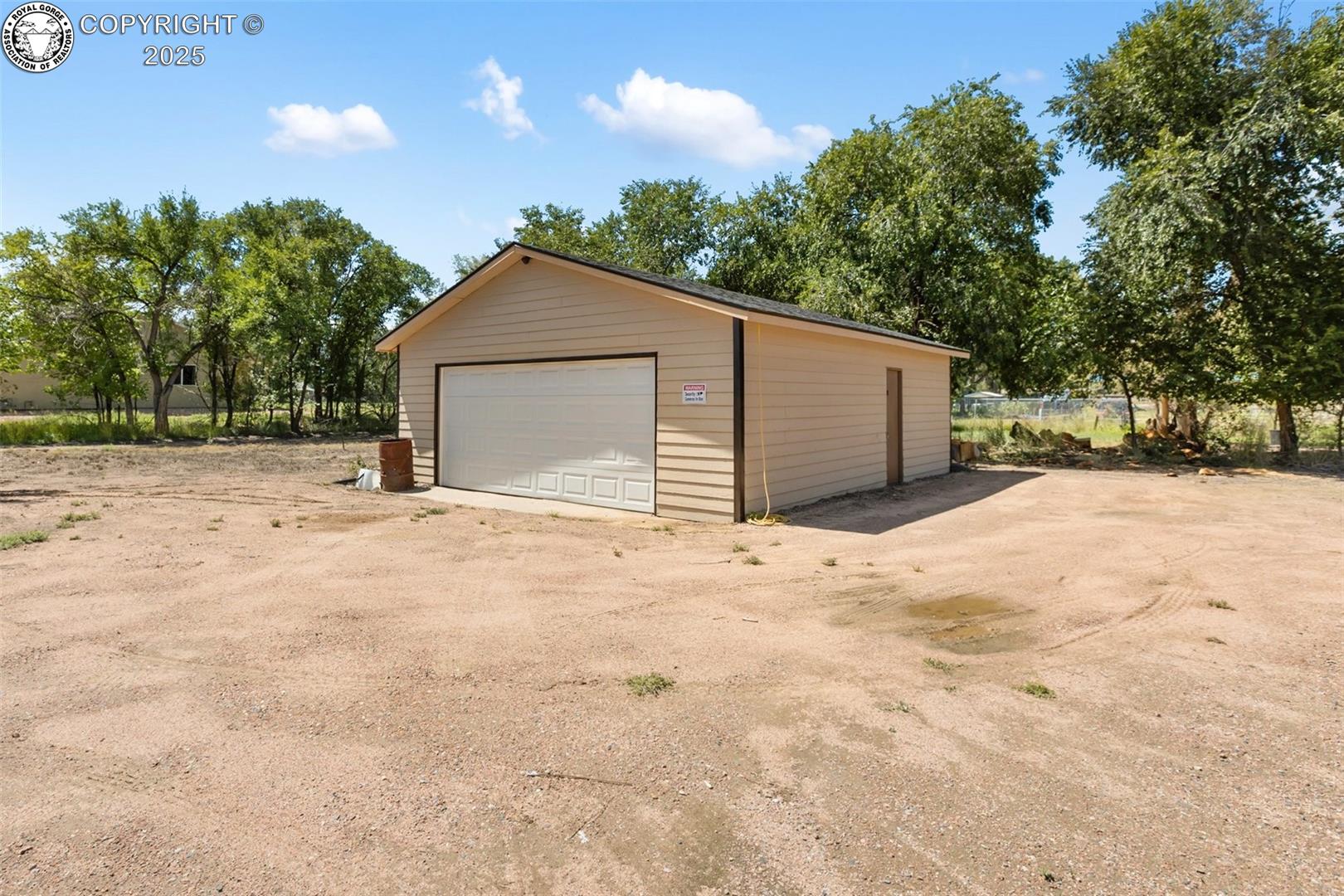 Detached beige garage with a white double door on a spacious gravel lot.