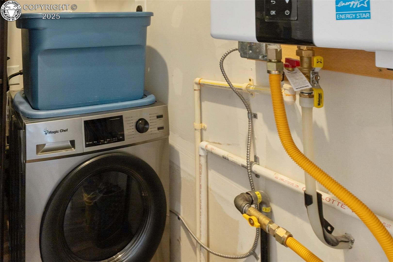 Laundry area with a front-loading washer beneath a blue bin beside a tankless water heater.