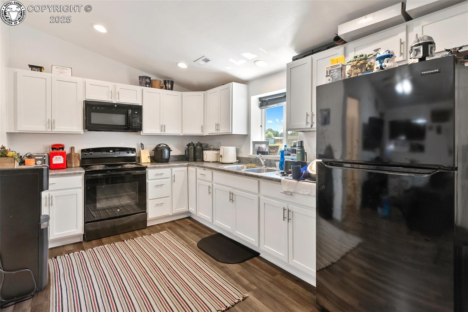 Kitchen with white cabinets, black appliances, dark countertops, and a striped floor rug.