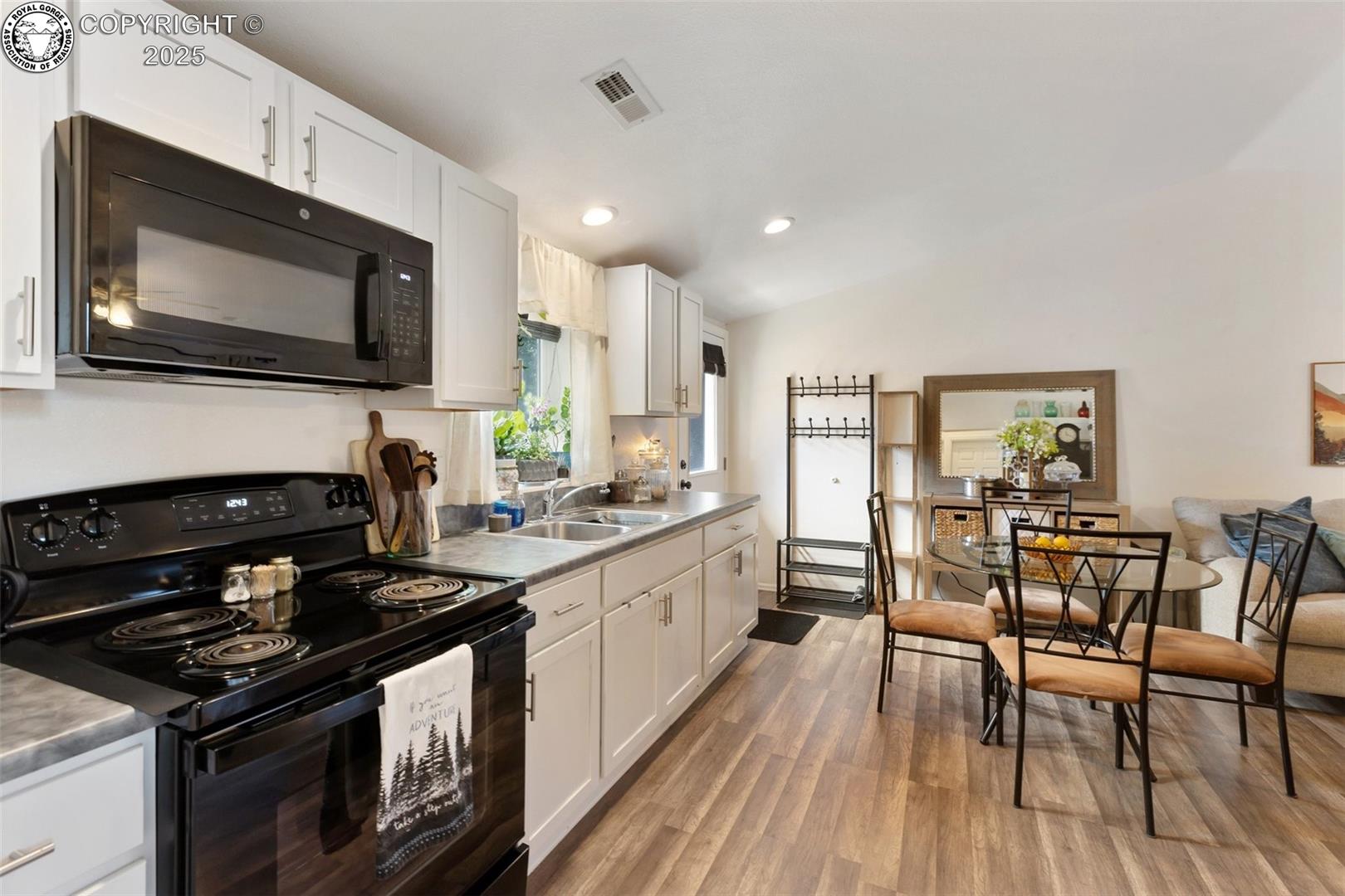 Kitchen with white cabinets and black appliances opening to a dining area with a round glass table.