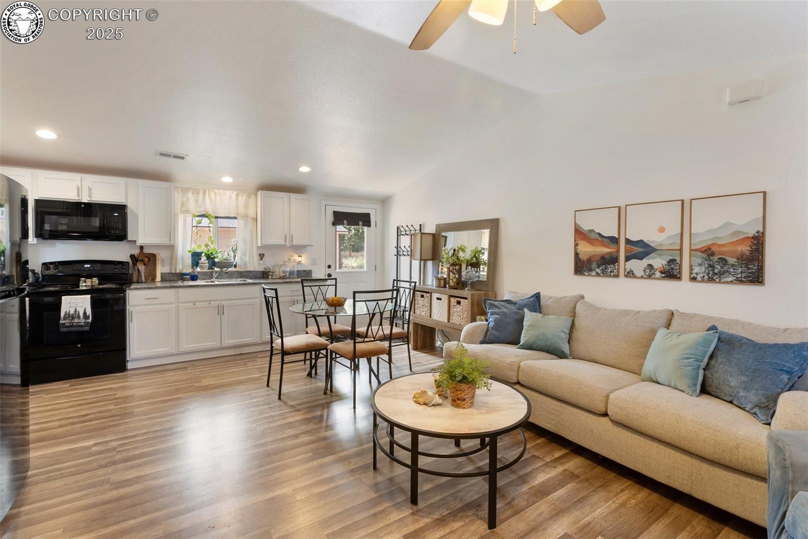 Open-plan living room and kitchen with a beige sectional, dining table, and white cabinetry.