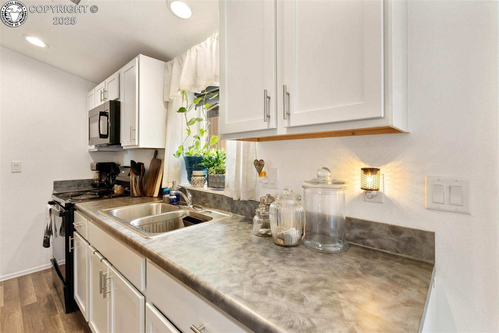 Kitchen with white cabinets, gray counters, a double-basin sink, and plants by the window.
