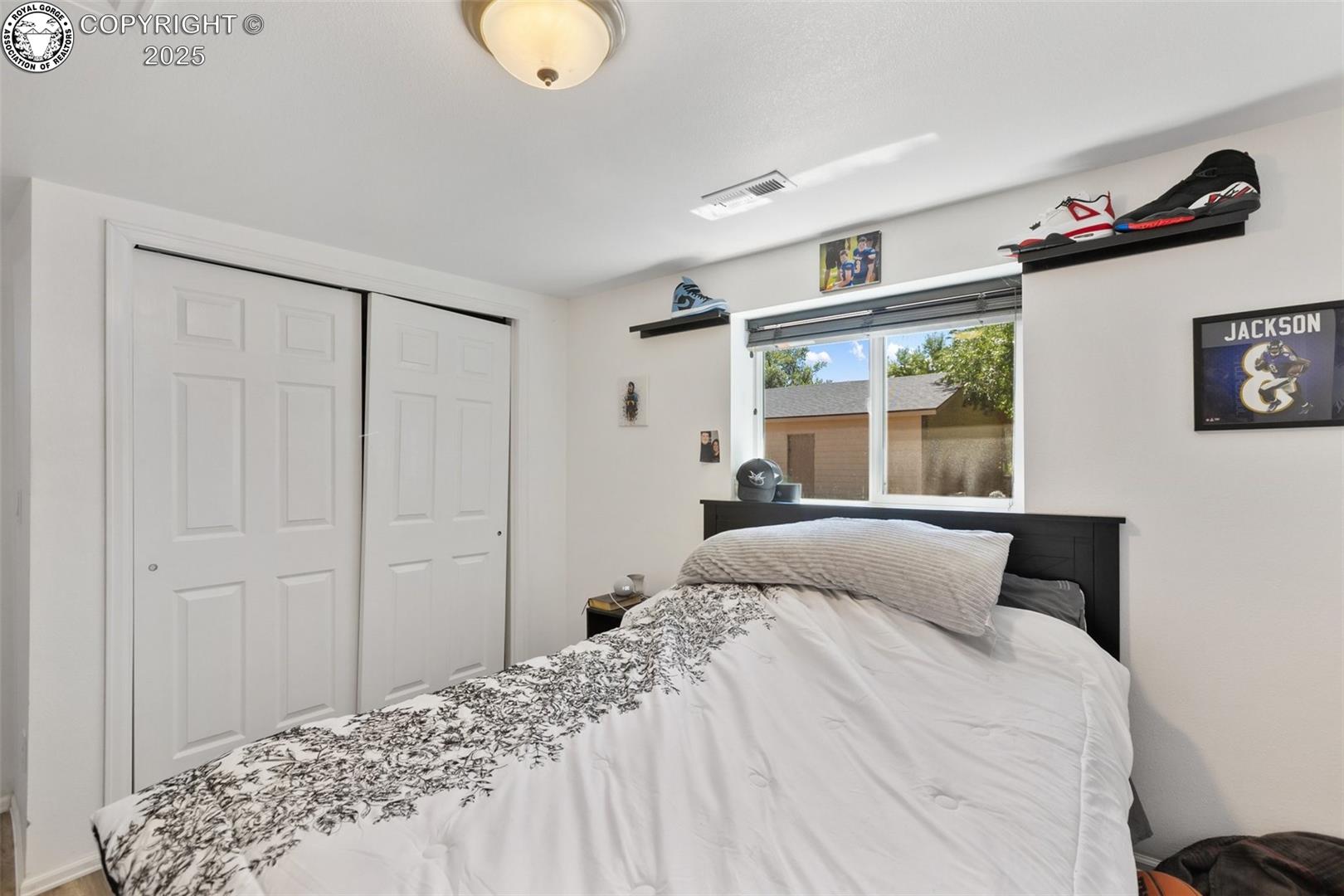 Bedroom with patterned white bedding, sliding closet doors, and sports memorabilia on wall shelves.