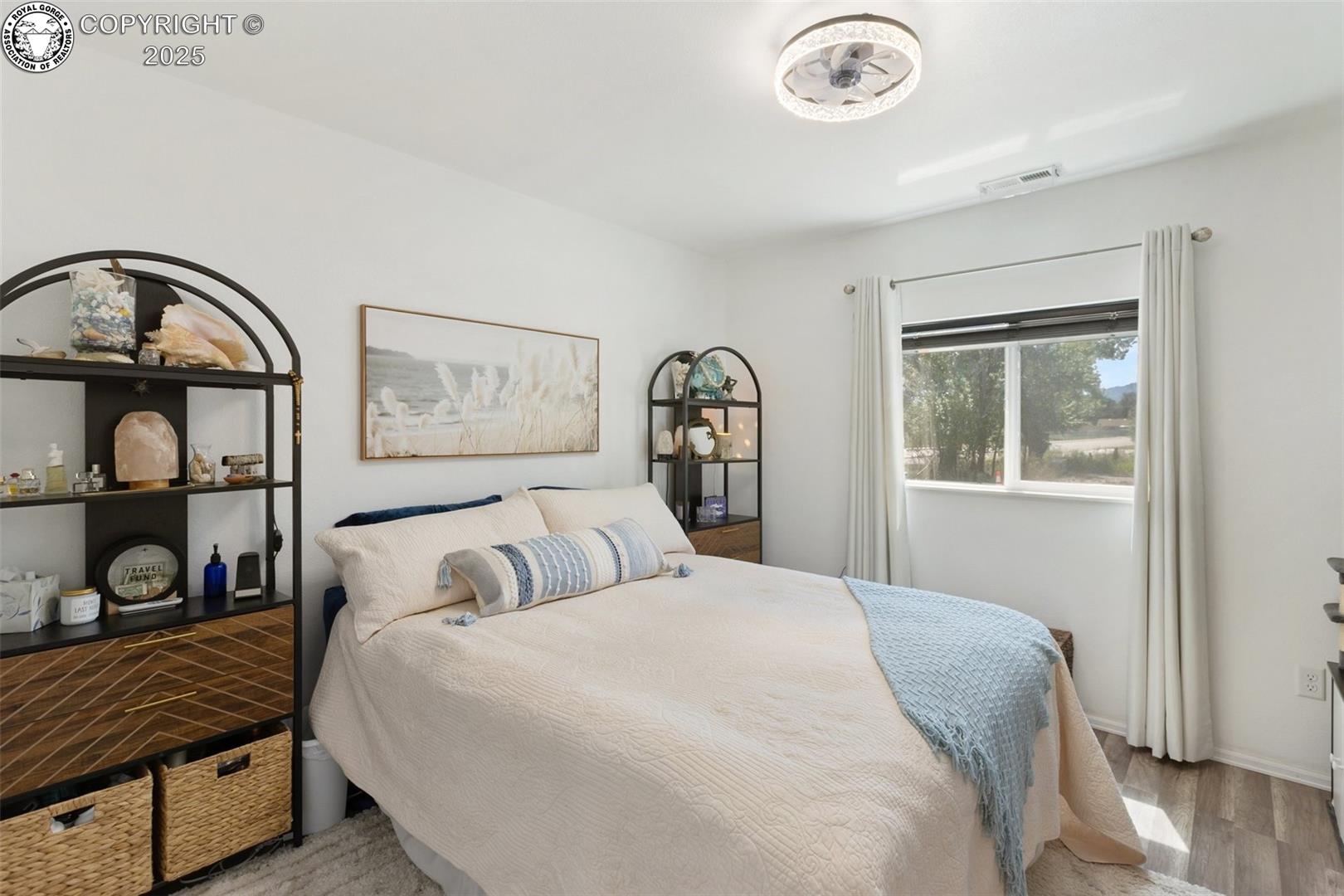 Bedroom with cream bedding, a light blue throw, arched display shelves, and a sunlit window.