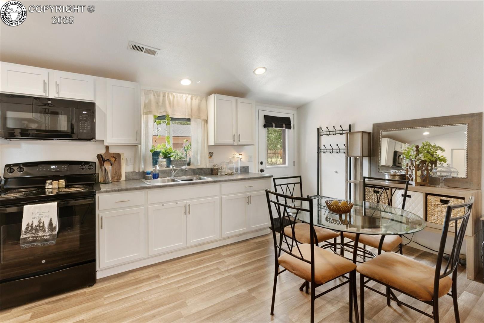 Kitchen and dining area with white cabinetry, black appliances, and a glass table with four chairs.