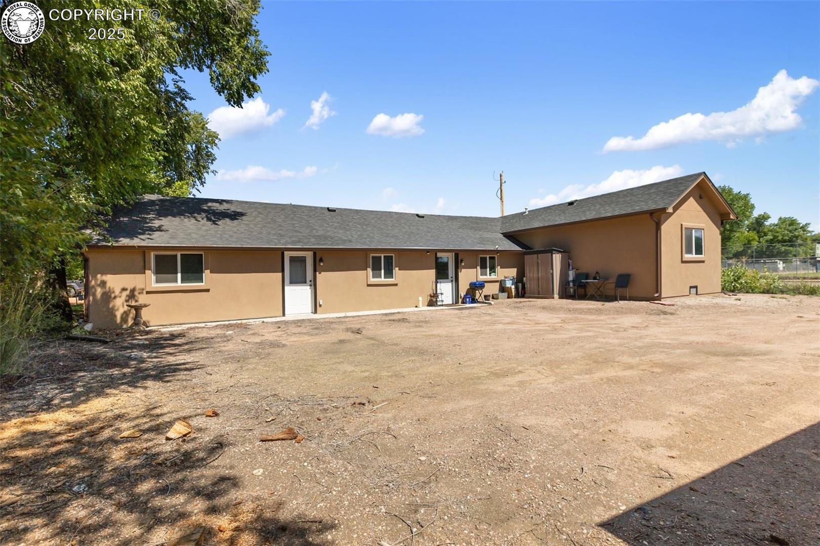 Tan home exterior with a long roofline, several doors, and a broad dirt yard.