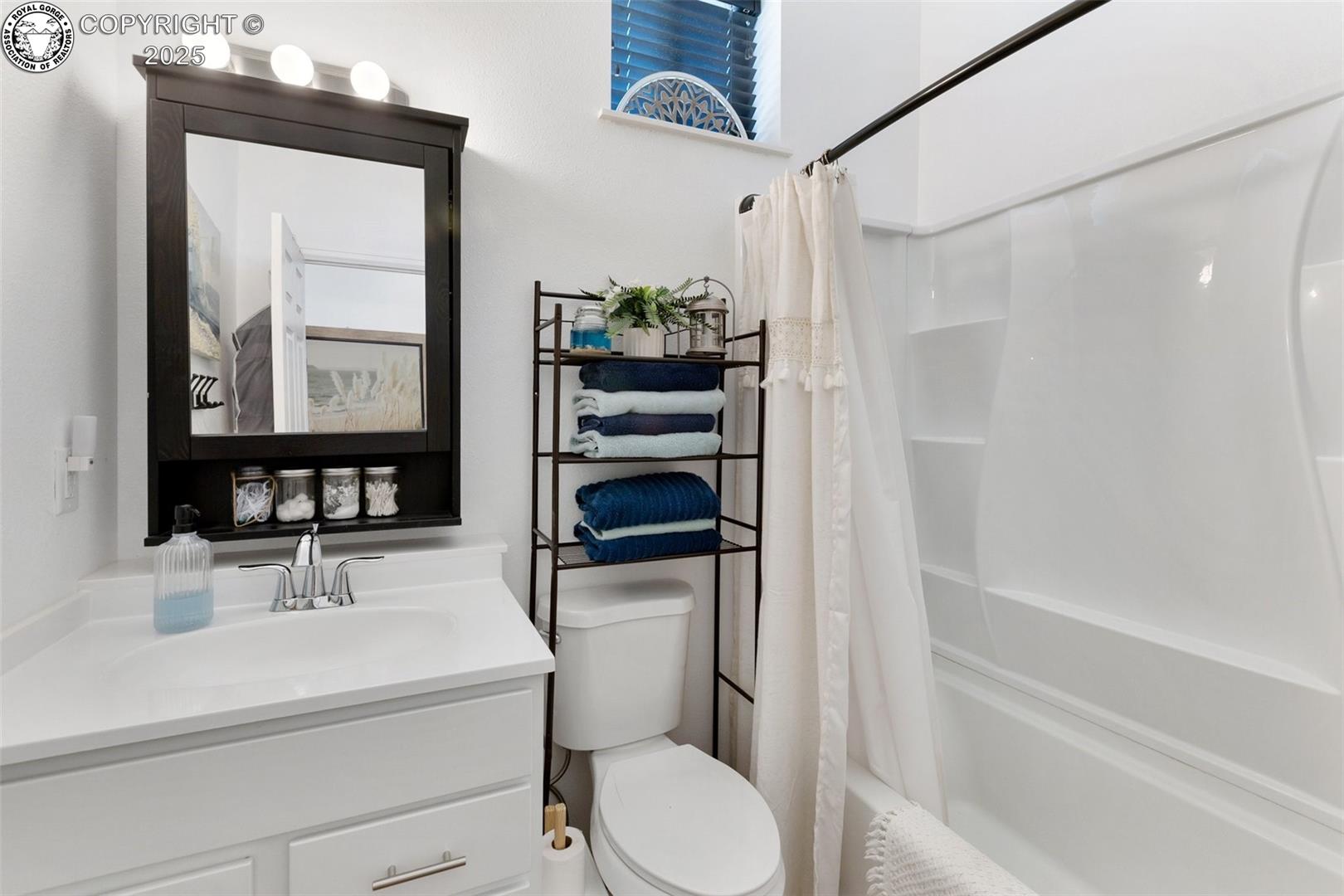 Bathroom with a white vanity, bathtub, and towels on open shelving.