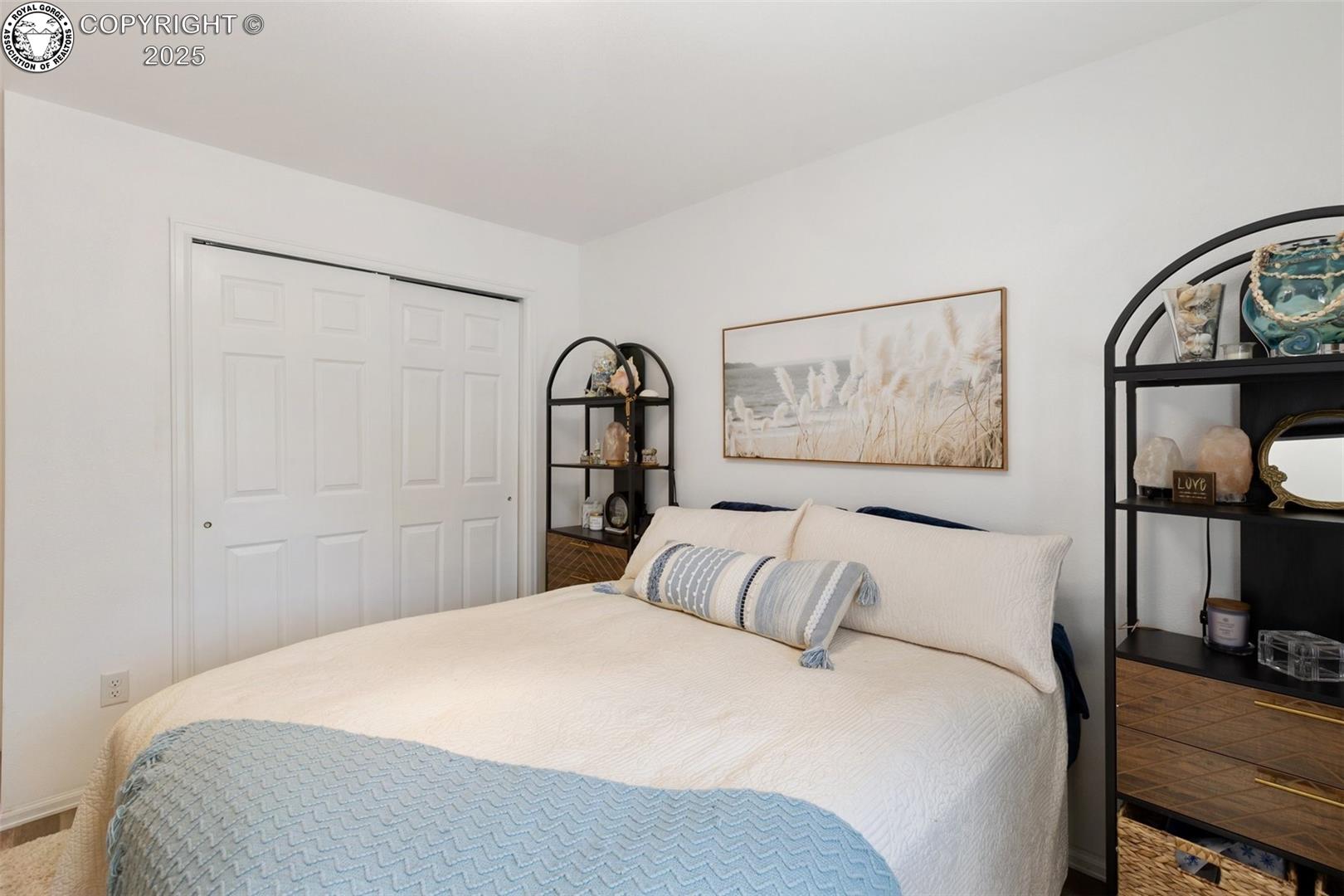 Bedroom with a white bed, blue throw, sliding closet doors, and black display shelves.