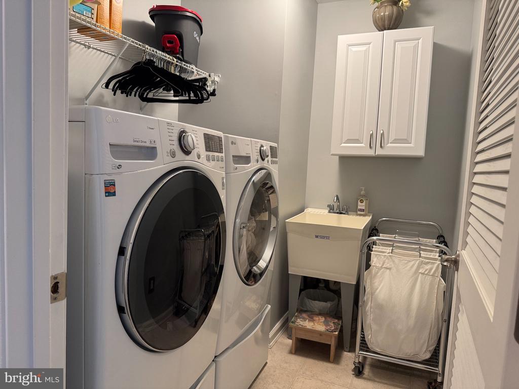 Laundry room with front-loading washer and dryer beside a utility sink and rolling hamper.