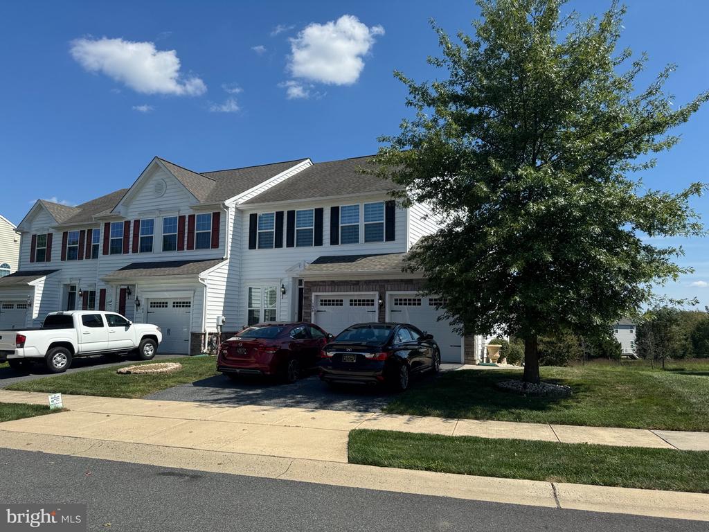 White two-story attached homes with garages, parked cars, and a large shade tree.