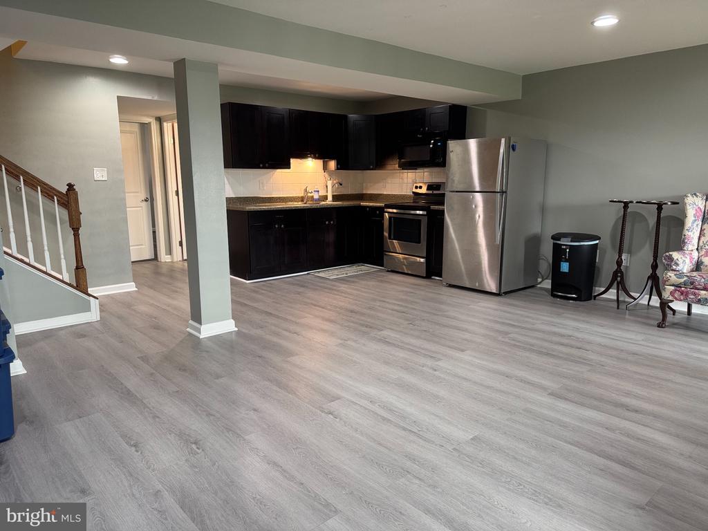 Open kitchen and living area with dark cabinets, stainless appliances, and gray plank flooring.
