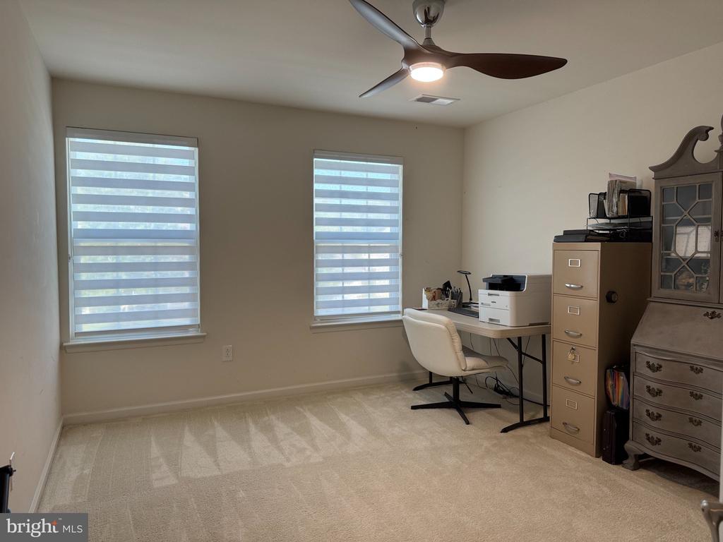 Home office with two striped-blind windows, a desk and printer, and a ceiling fan.