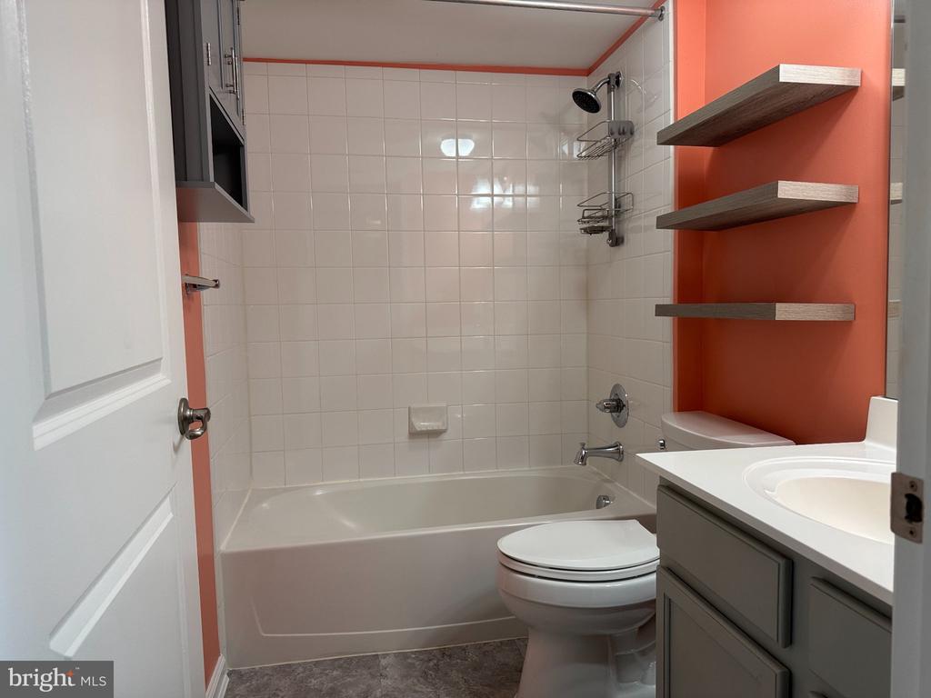 Bathroom with white tub, tiled walls, gray vanity, and coral accent wall.