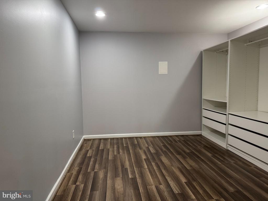 Empty walk-in closet with built-in white shelving and drawers and dark plank flooring.