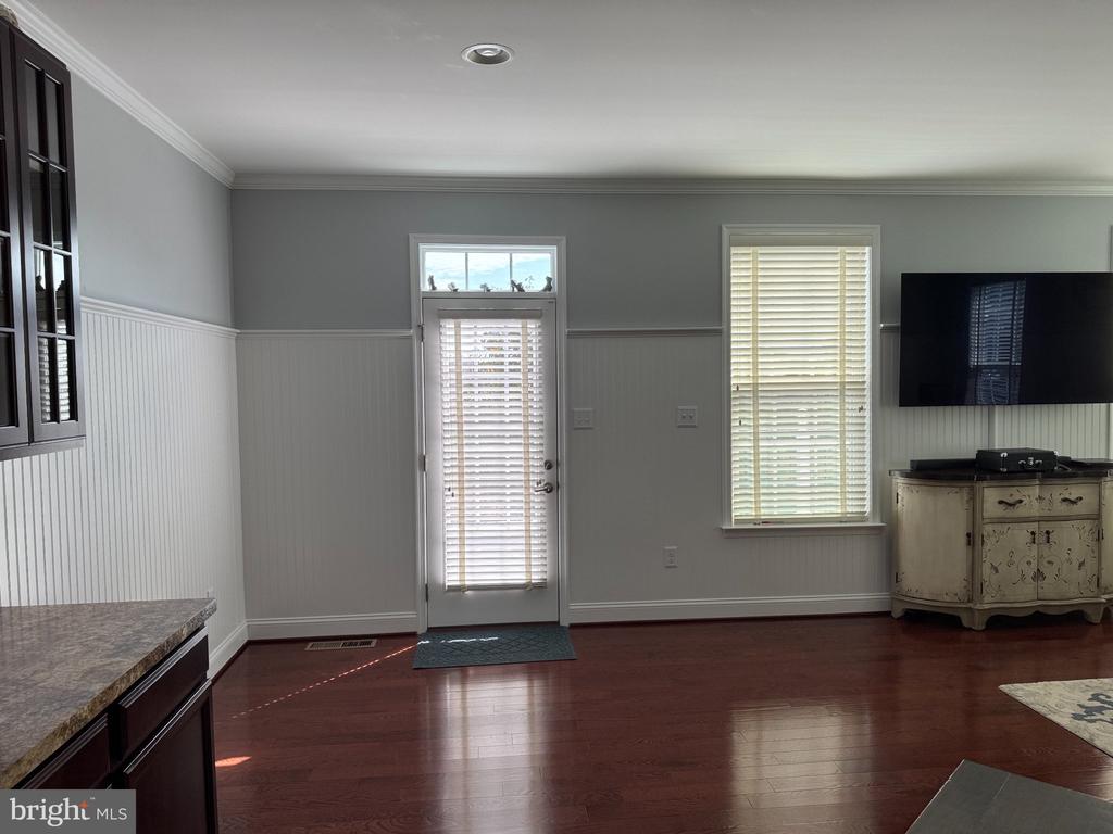 Living room with hardwood floors, beadboard wainscoting, a window, and a glass-paneled door with blinds.