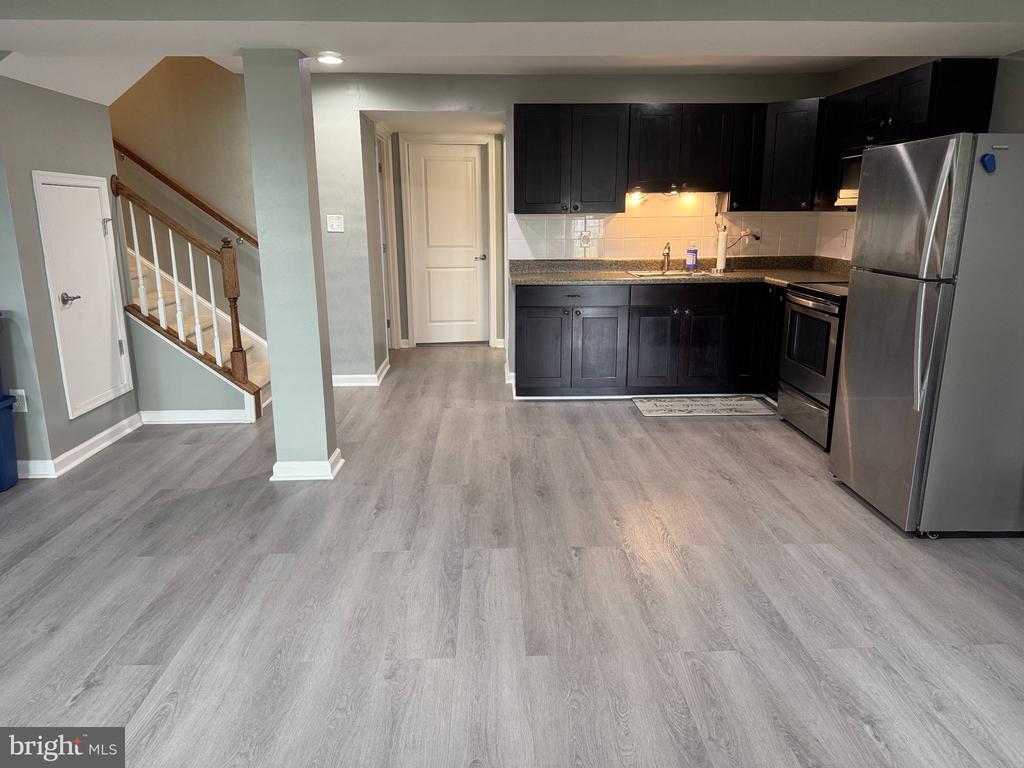 Kitchen with dark cabinets and stainless steel appliances, open to a staircase and hallway.