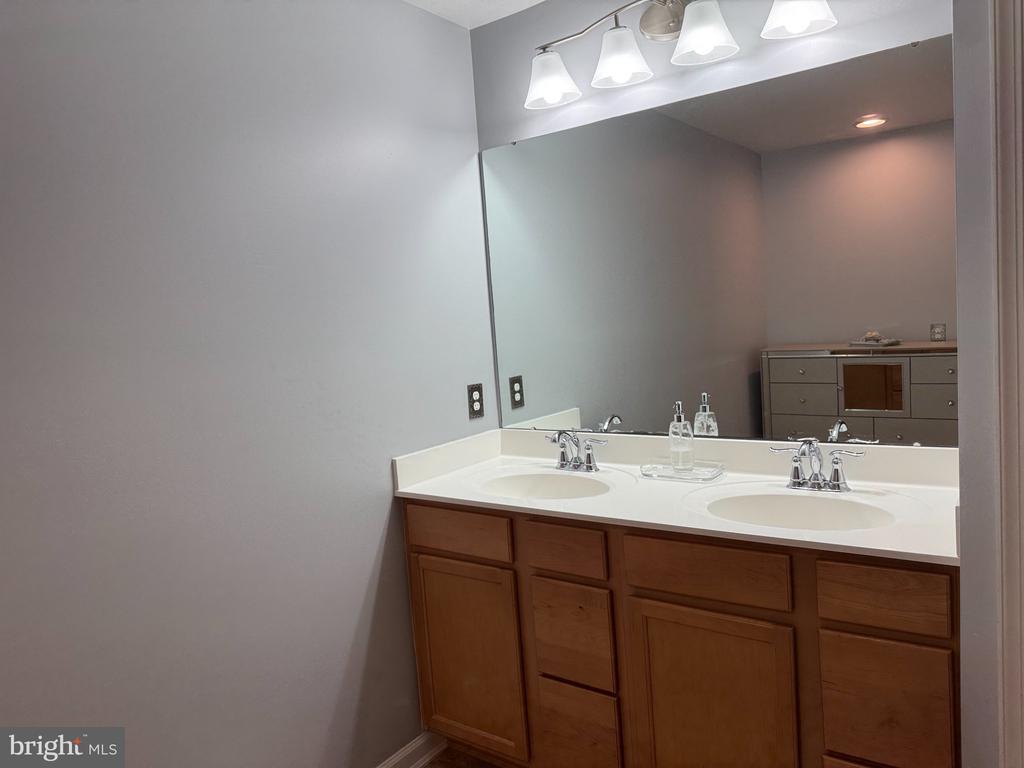 Bathroom with a double-sink vanity, white countertop, wood cabinetry, and a large mirror.
