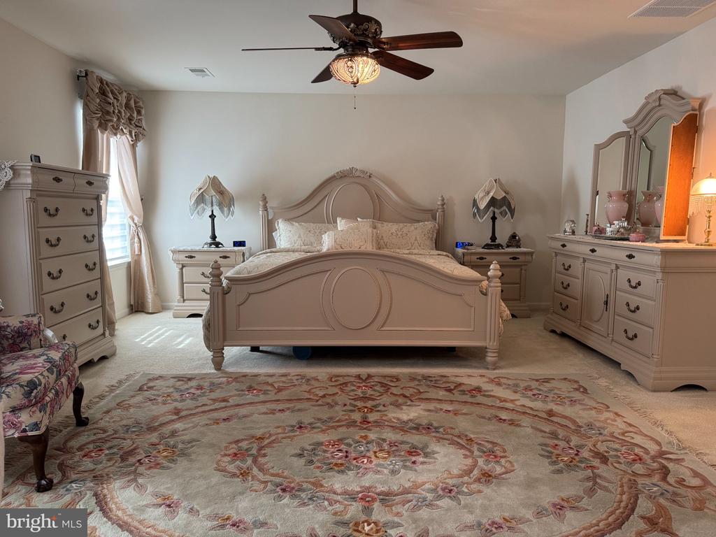 Bedroom with an ornate cream bed, matching furniture, ceiling fan, and floral rug.