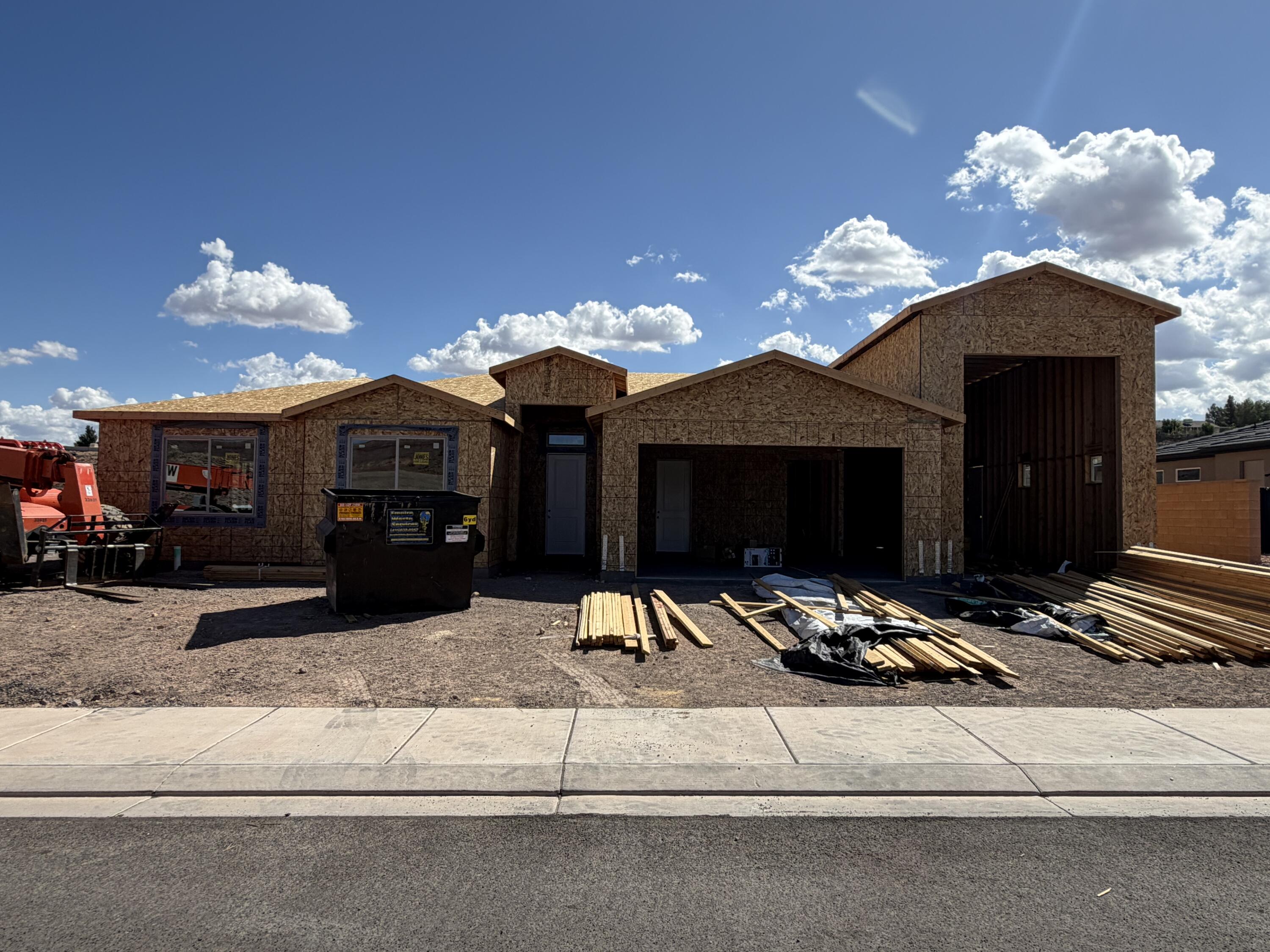 House under construction with exposed sheathing, open garage bays, and building materials in the yard.