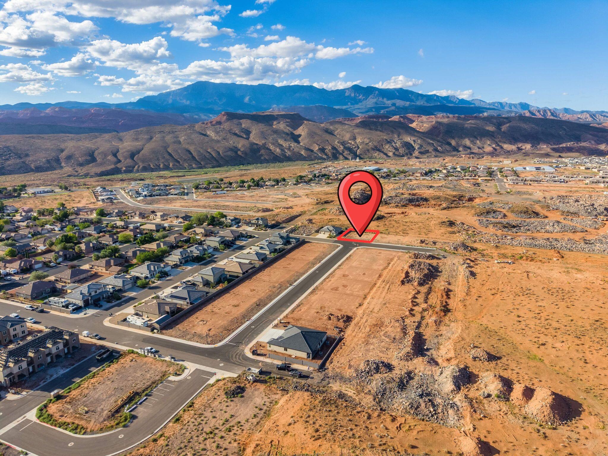Aerial view of a marked vacant lot beside new homes, with desert mountains beyond.