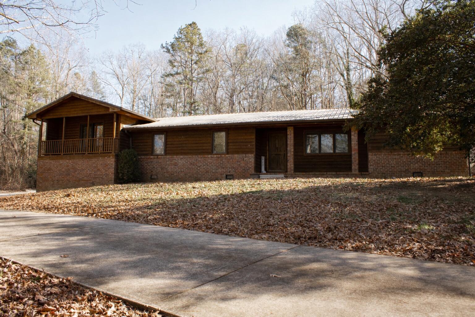 Wood-sided and brick house with a raised porch, leaf-covered yard, and concrete driveway.