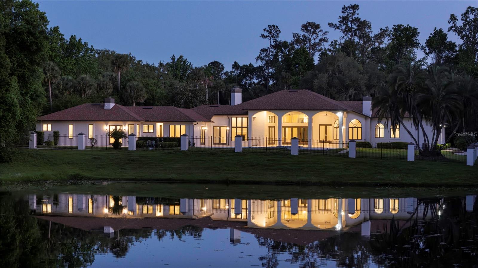 Illuminated white home beside a pond, reflected in the water at dusk.
