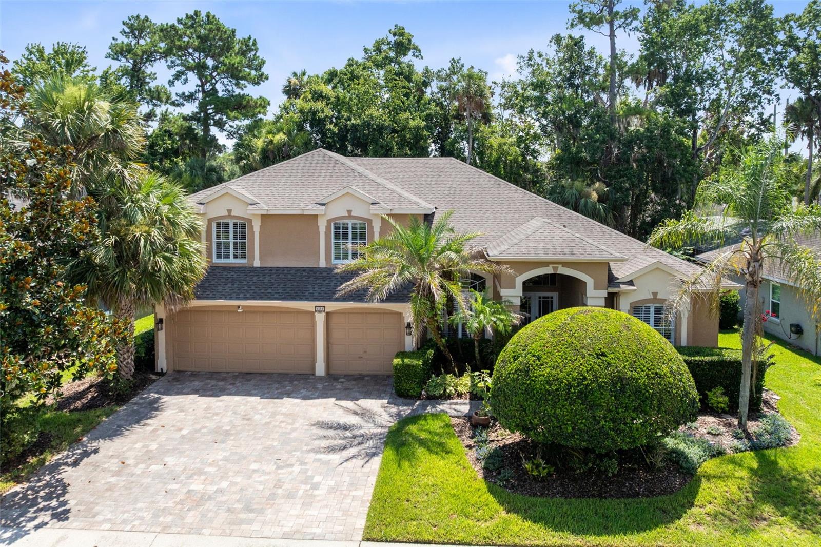 Tan two-story home with a three-car garage, arched entry, and landscaped front yard.