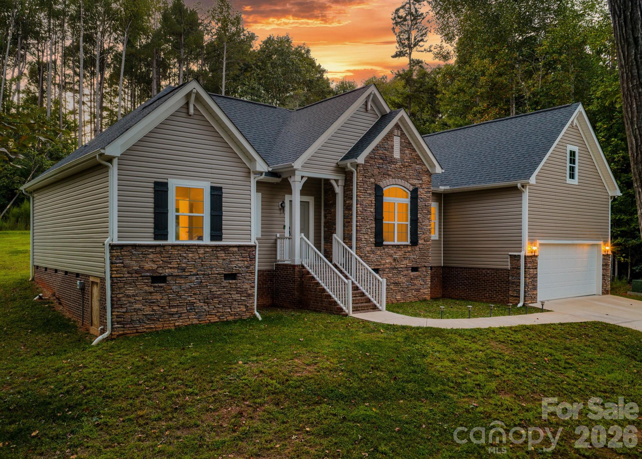 One-story beige house with stone accents, front porch, and attached garage at sunset.