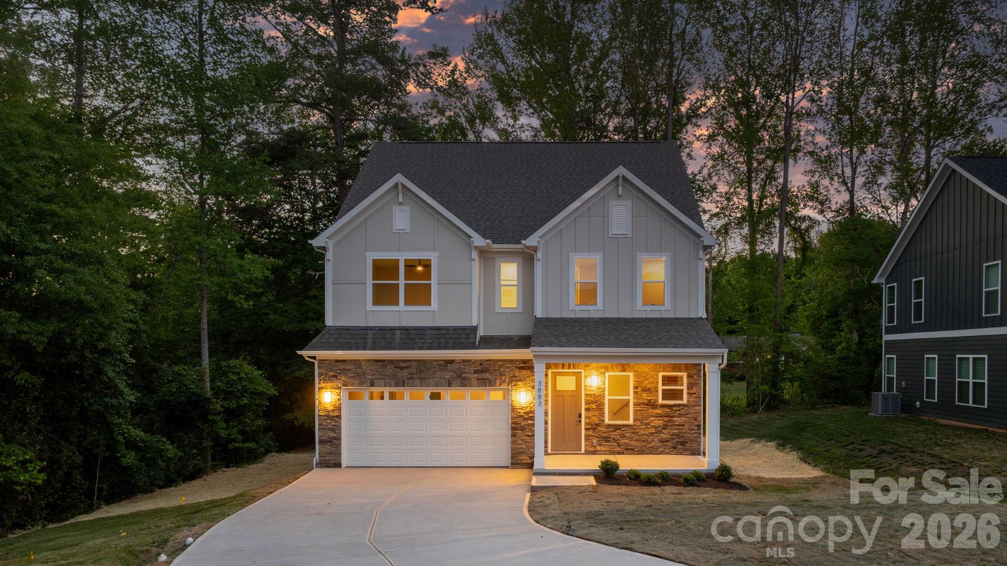 Two-story gray home with stone facade and illuminated windows at dusk.