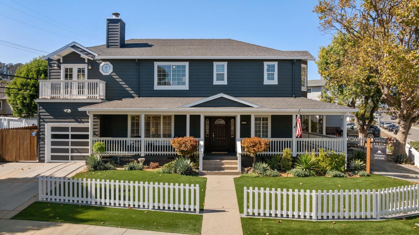 Two-story dark blue San Bruno home with a covered porch, attached garage, and white picket fence.