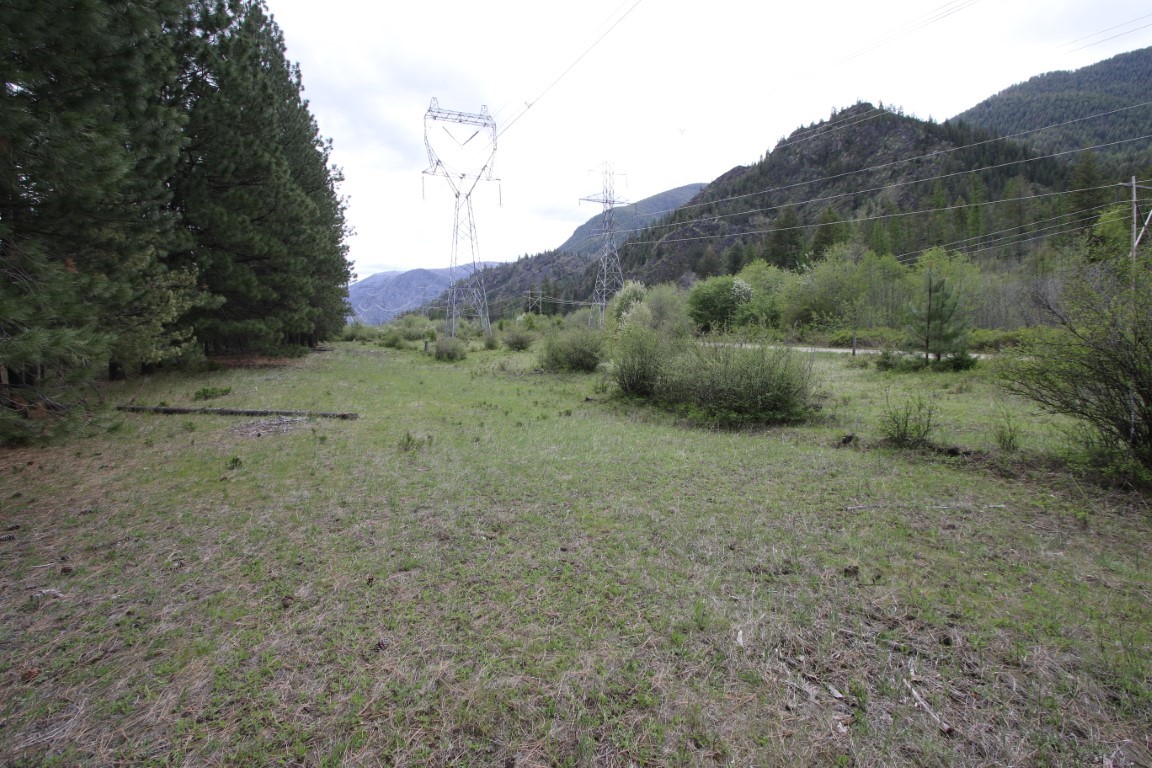 Vacant grassy parcel with shrubs, transmission towers, and forested mountains beyond.