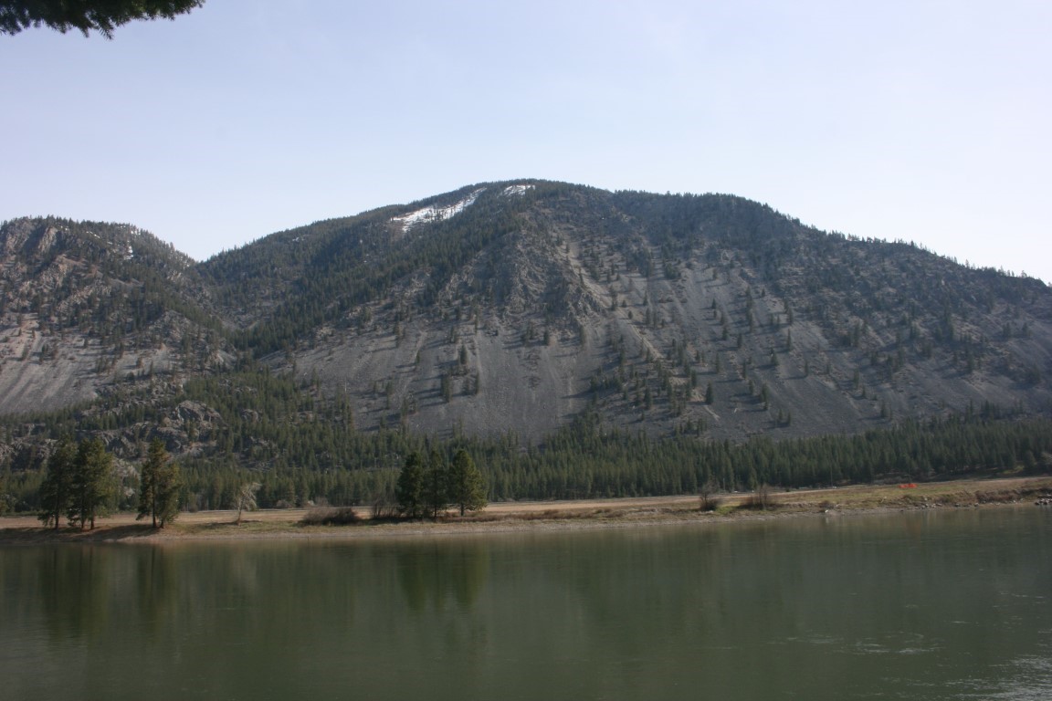 Riverfront landscape with a broad rocky, forested mountain rising across the water.