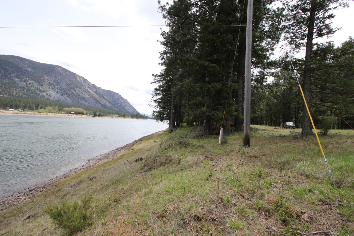 Riverside land with a grassy bank, wooded shoreline, and mountain across the water.
