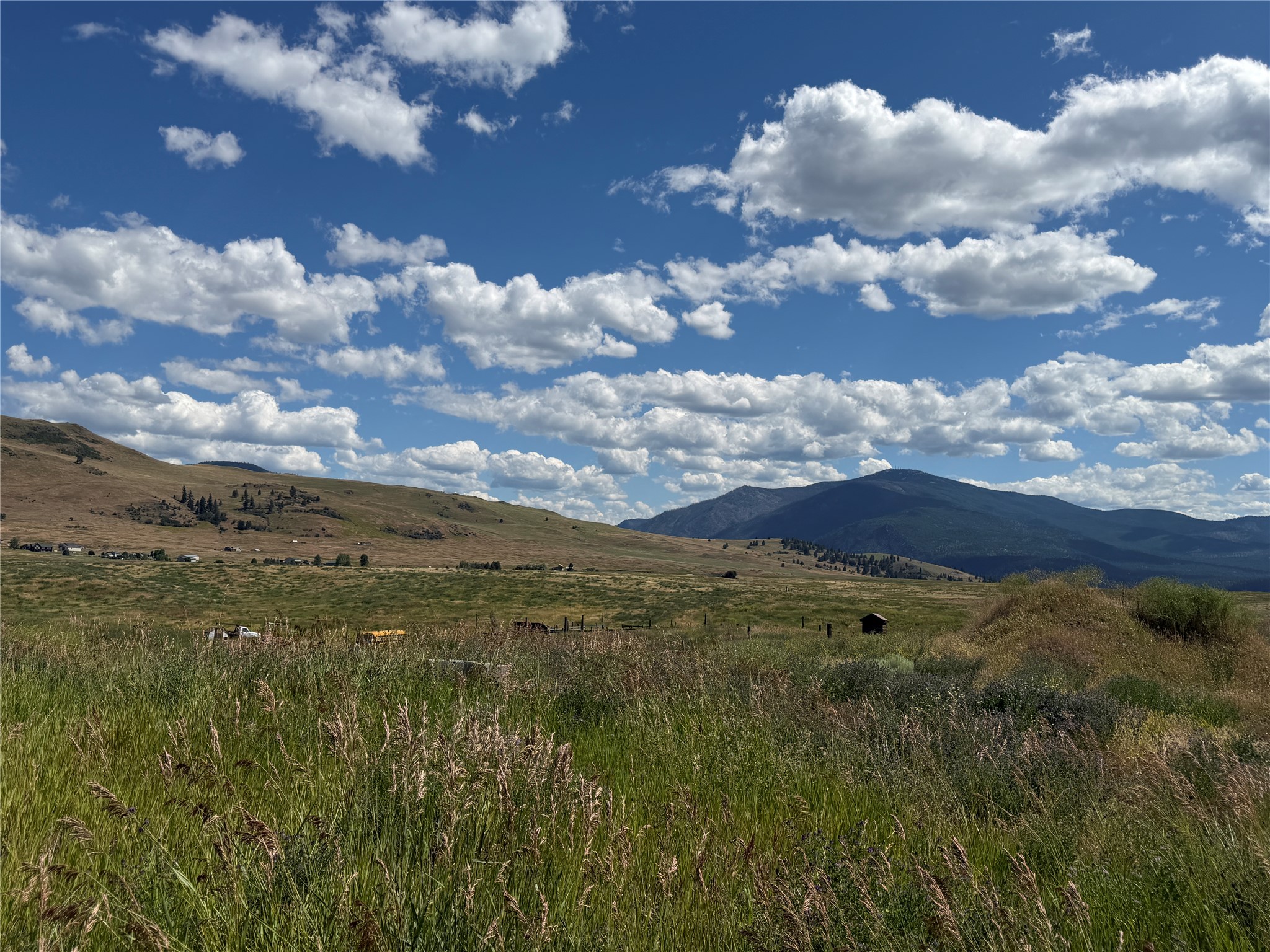 Open grassy land and rolling hills stretch toward distant mountains beneath a cloud-filled sky.