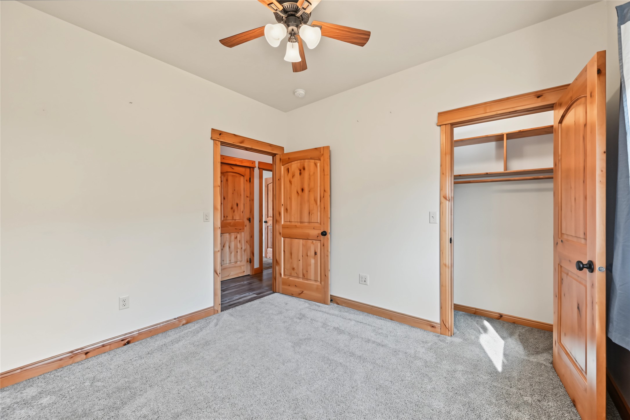 Empty bedroom with gray carpet, a ceiling fan, and an open closet framed in natural wood.