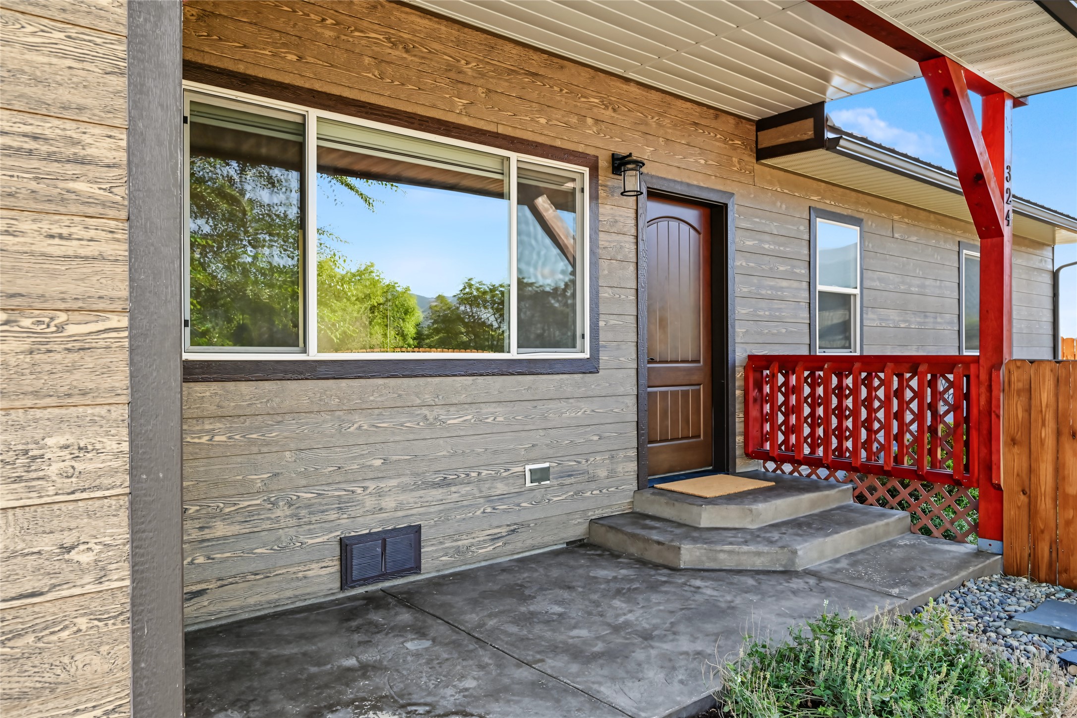 Home entrance with gray wood siding, concrete steps, and a covered porch with red railing.