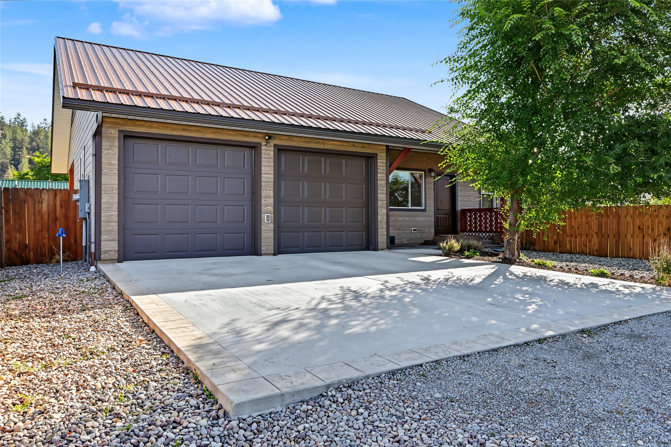 House exterior with two garage doors, a metal roof, and a wide concrete driveway.