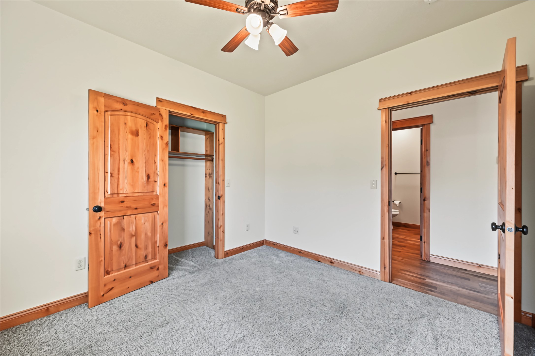 Empty bedroom with gray carpet, wood-trimmed doors, an open closet, and a bathroom doorway.