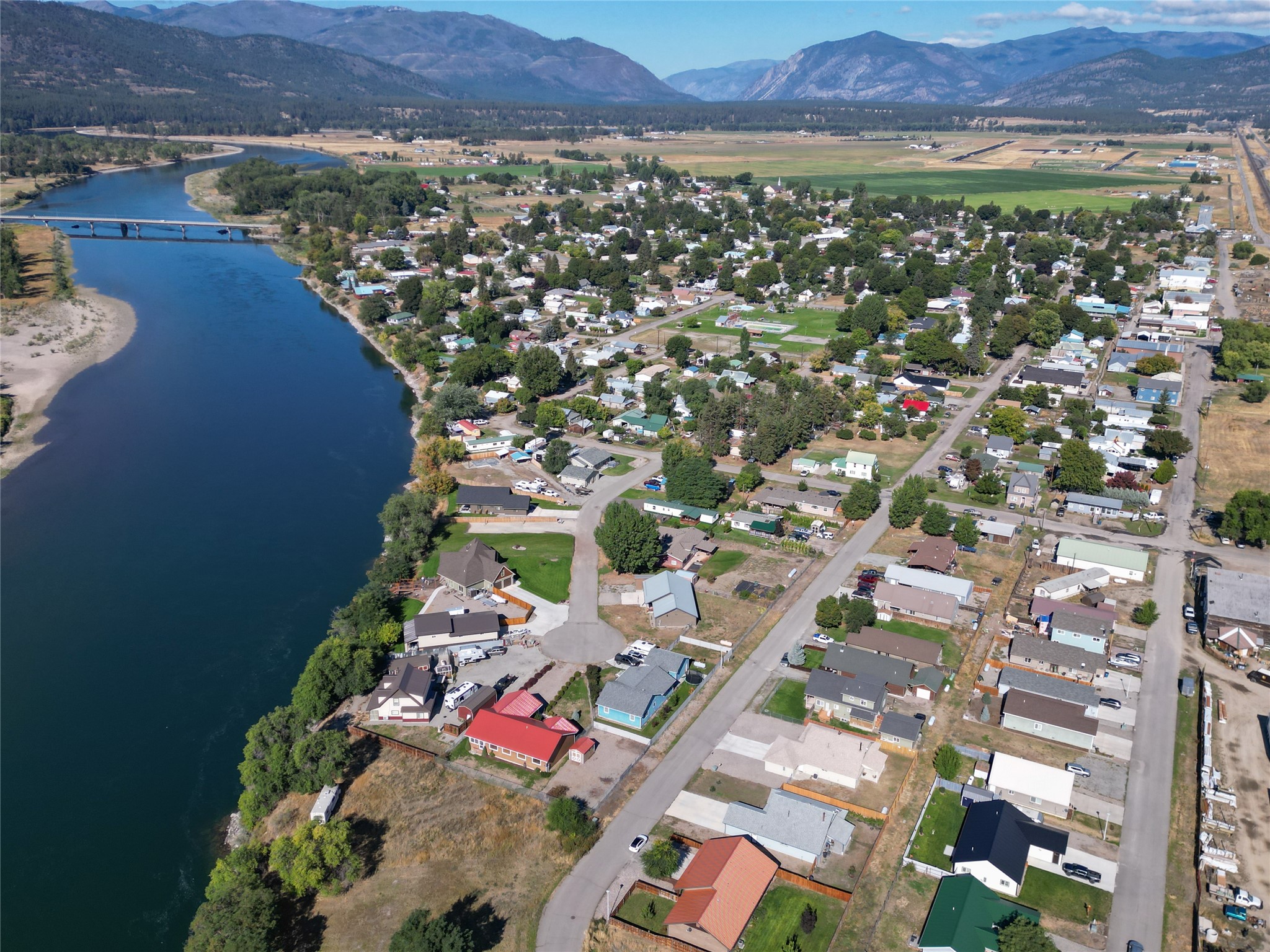 Aerial view of a riverside town with a bridge and mountains beyond.