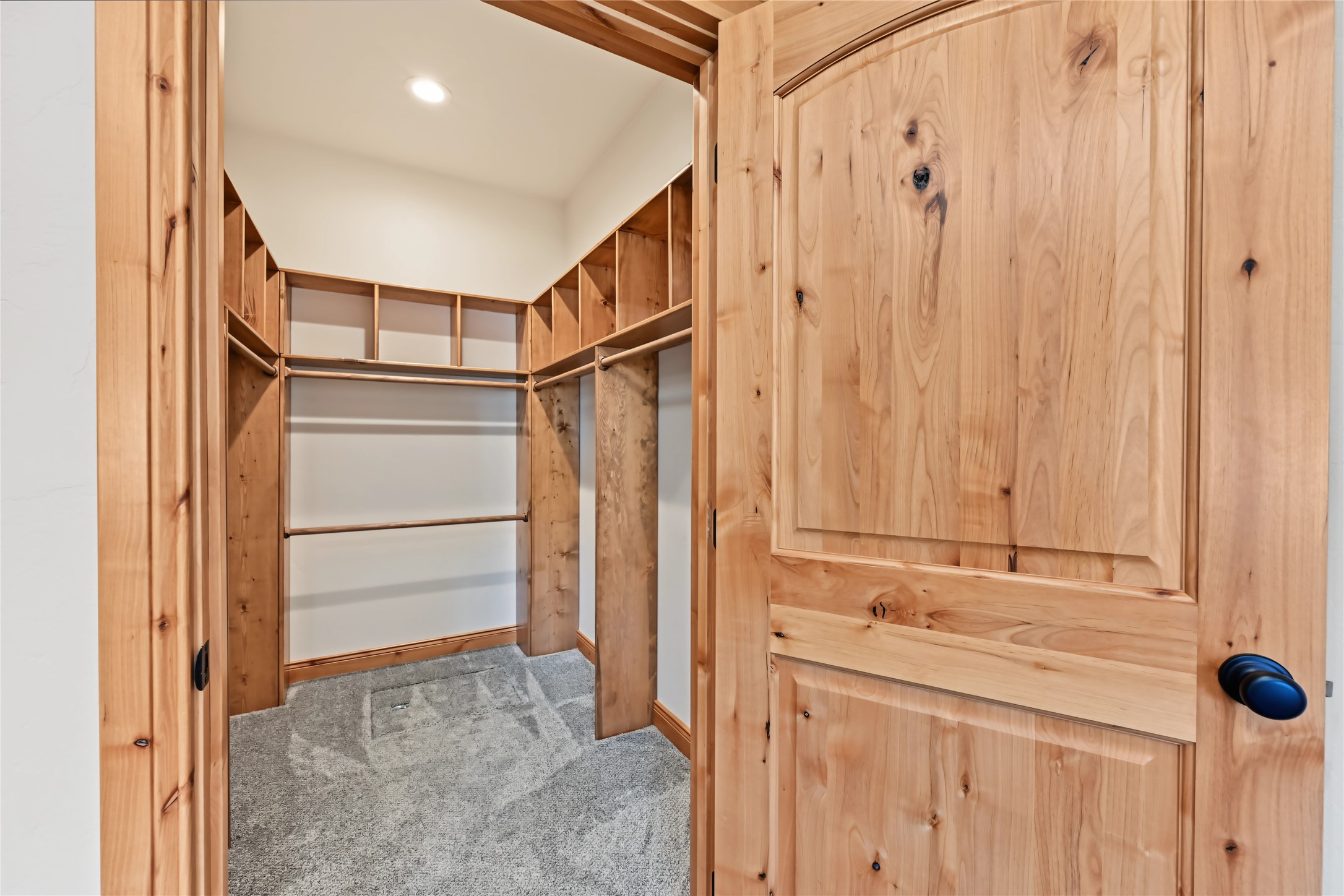 Walk-in closet with built-in wooden shelving and hanging rods, viewed through an open wood door.