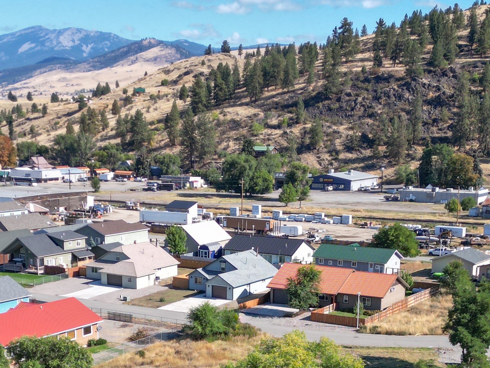 Aerial view of a Montana town below a pine-covered hillside and distant mountains.