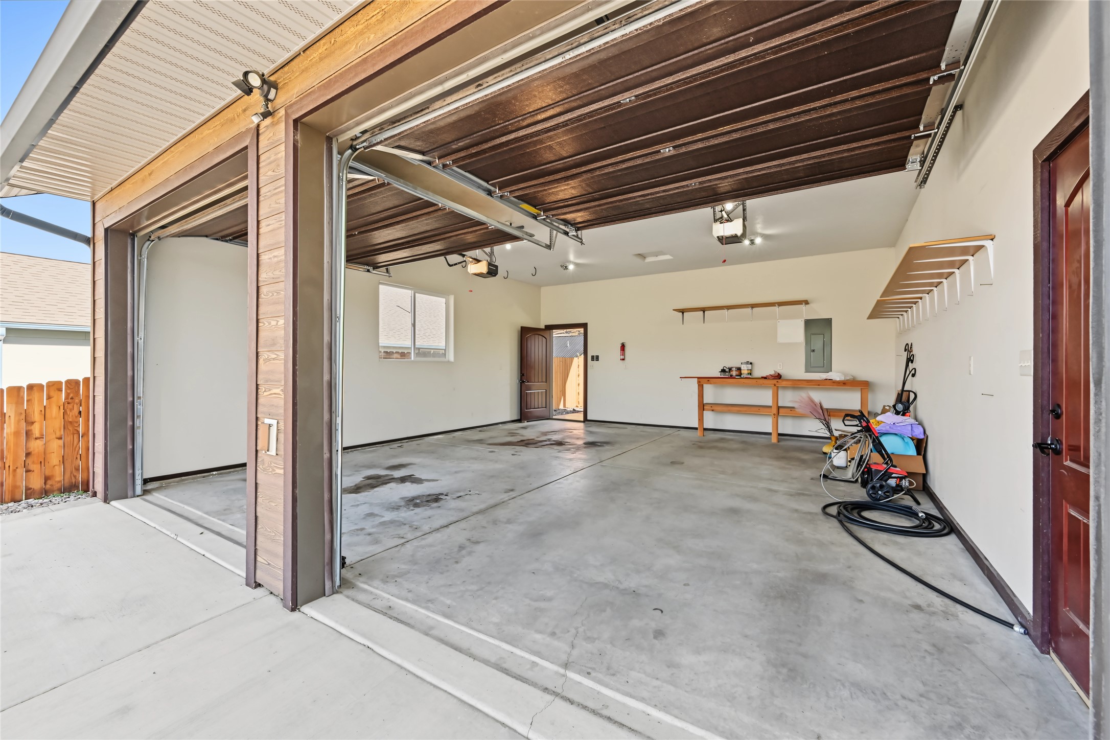 Two-car garage with open overhead doors, wall storage racks, and a wooden workbench.