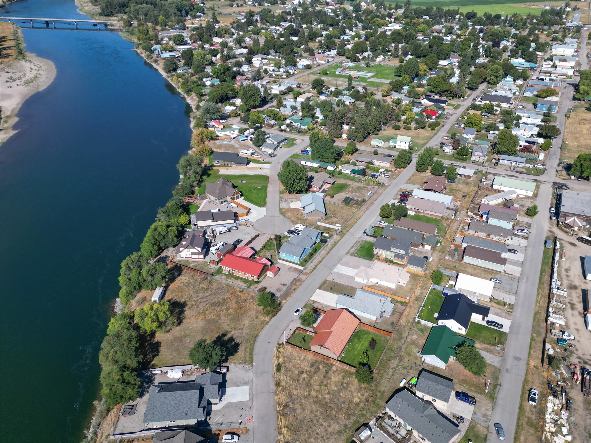 Aerial view of riverside homes and neighborhood streets, with a bridge crossing the river in the distance.