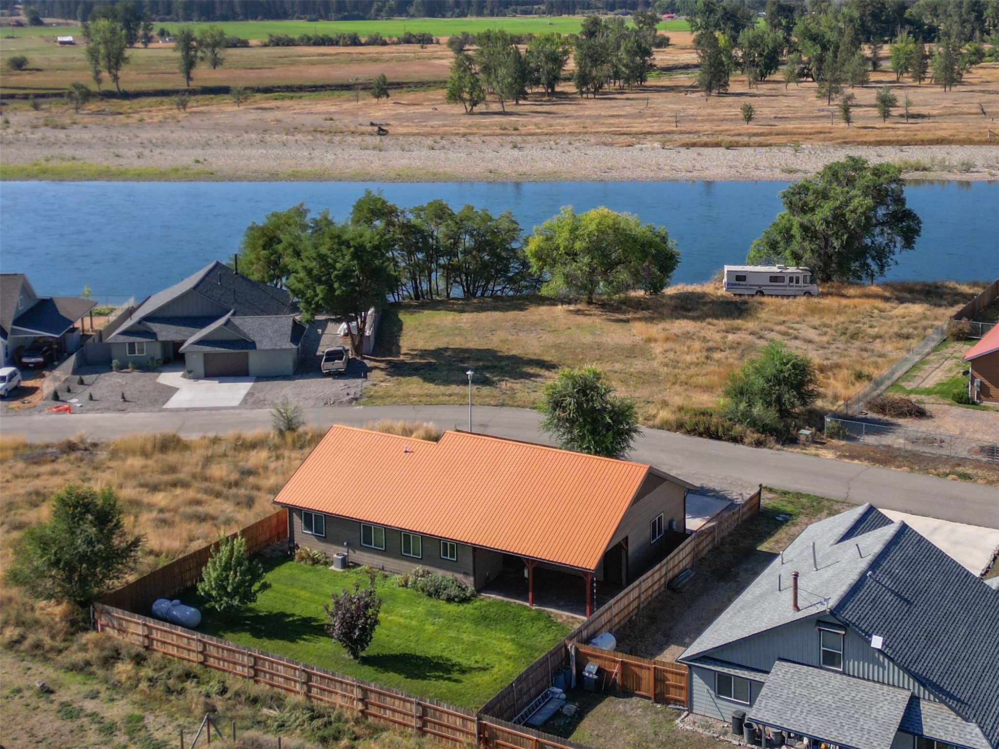 Aerial view of a home with an orange roof and fenced lawn beside a river.