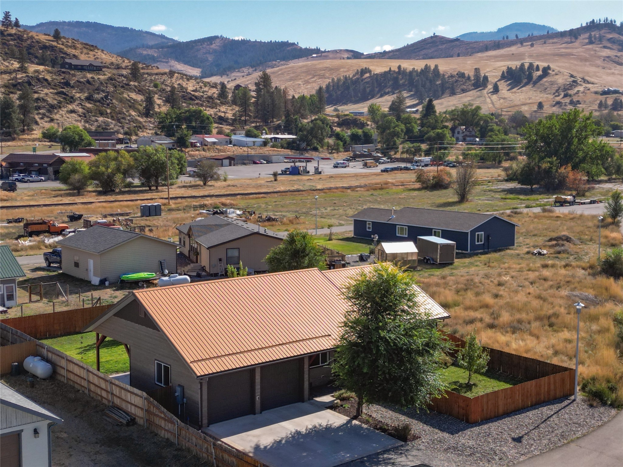 Fenced home with a copper-colored roof, surrounded by neighboring houses and rolling hills.