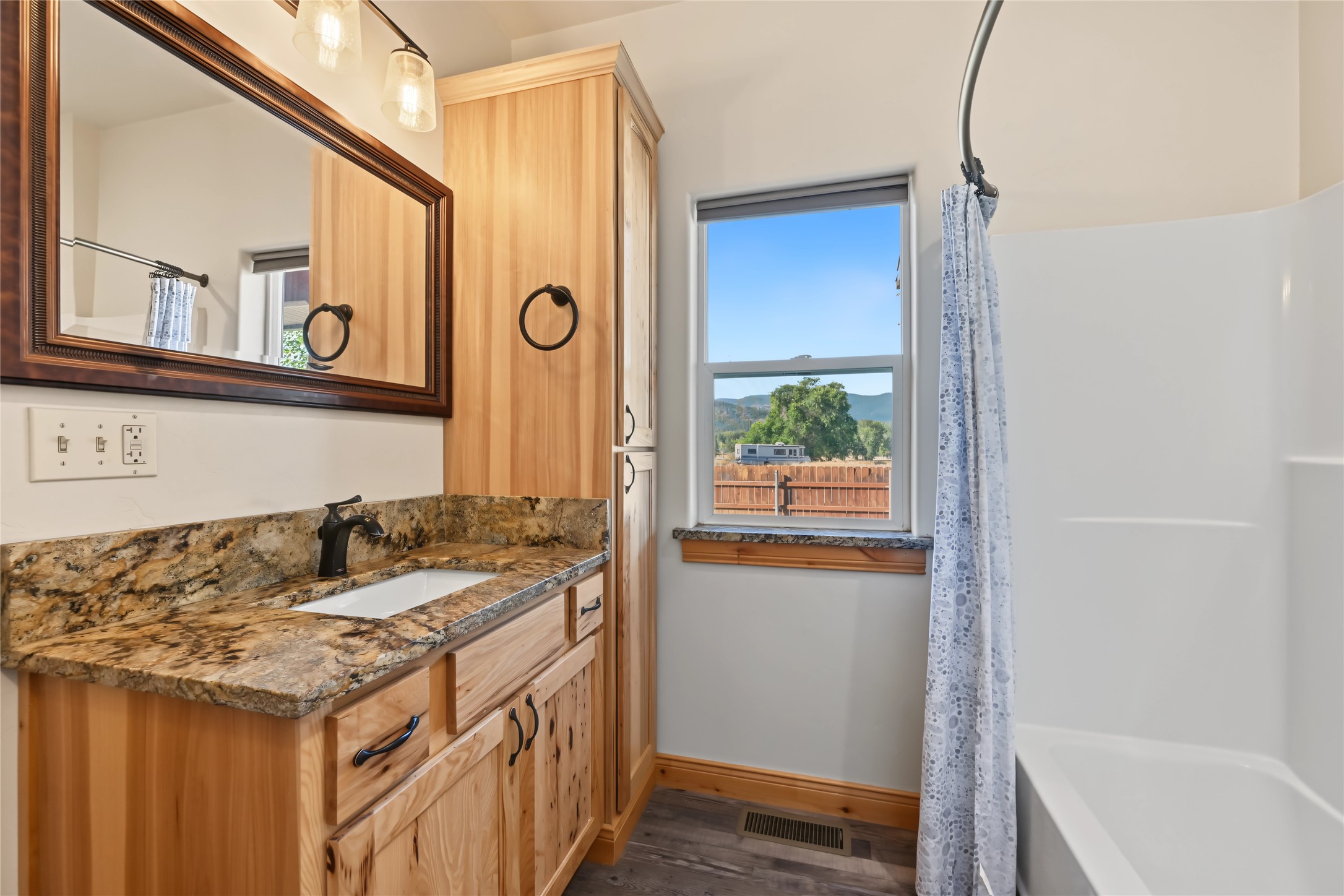 Bathroom with a wood vanity and stone counter, bathtub, and window overlooking distant hills.
