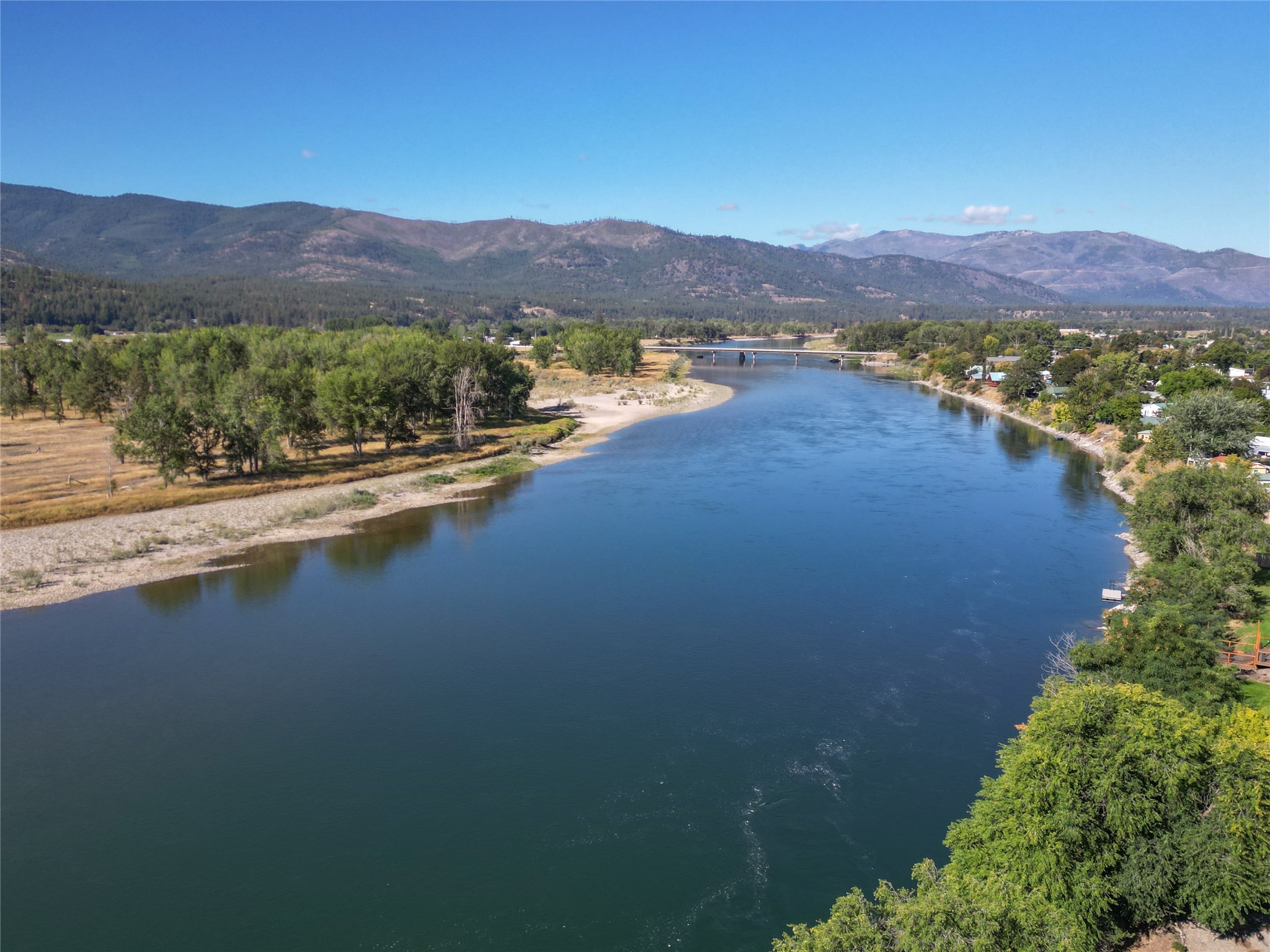 Broad river winding past a riverside town, with a bridge and mountains beyond.