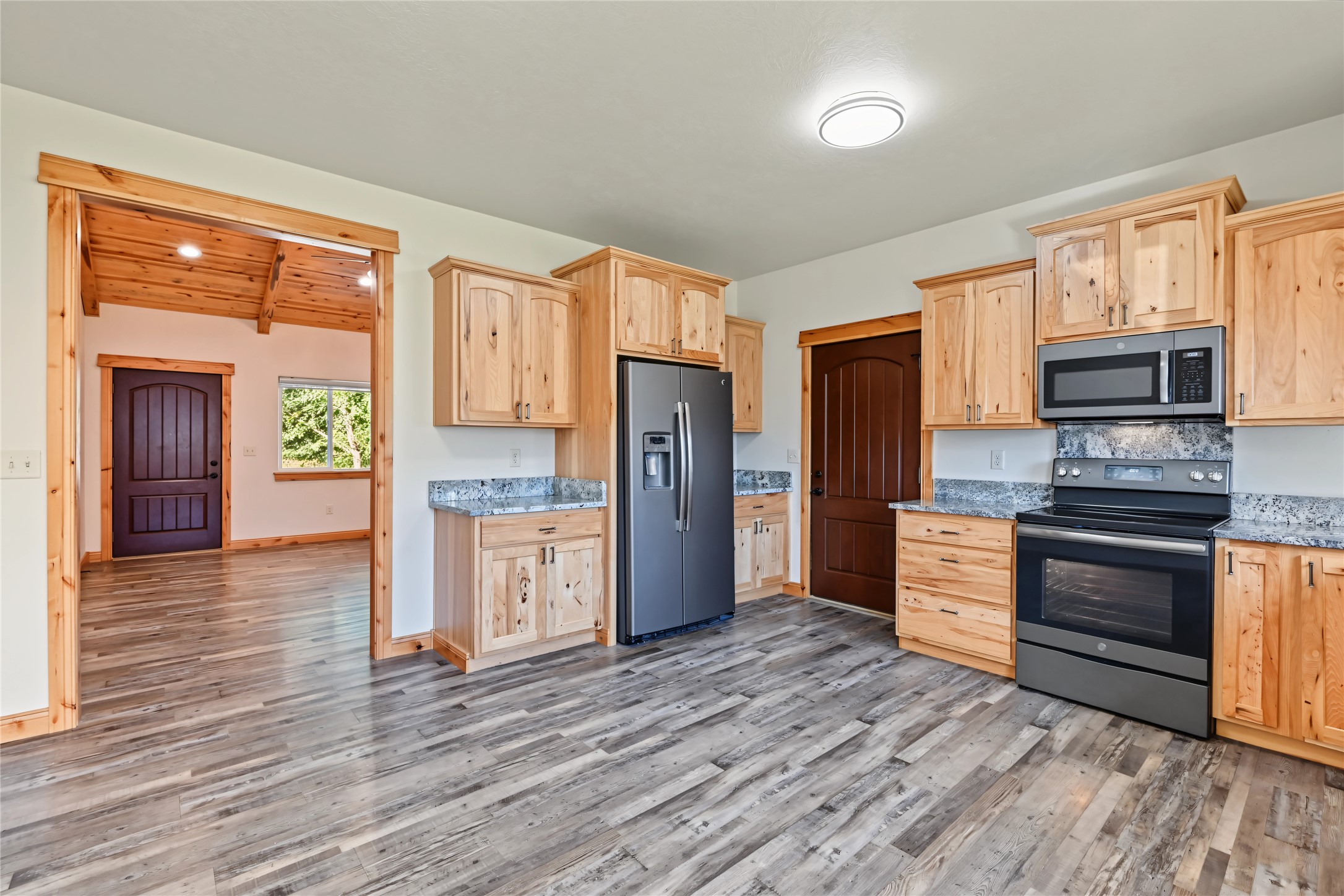 Kitchen with knotty-wood cabinets, gray counters, stainless appliances, and gray wood-look flooring.