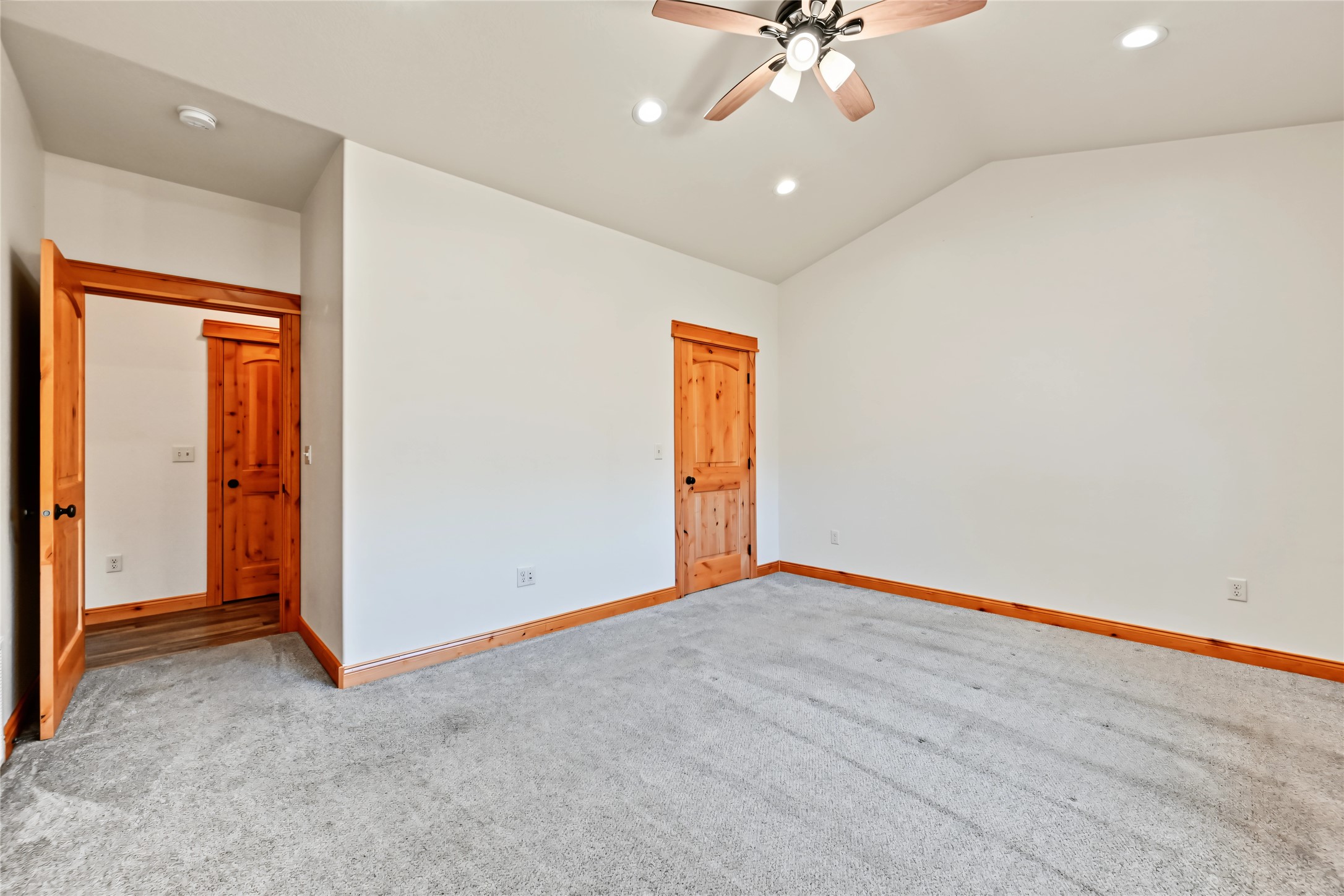 Empty bedroom with gray carpet, natural wood doors and trim, and a ceiling fan.