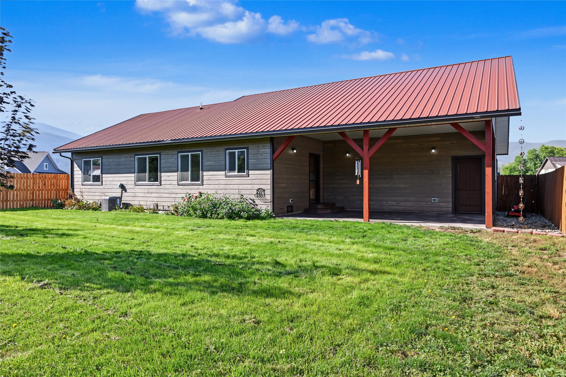 Home exterior with a red metal roof, covered patio, and broad green lawn.